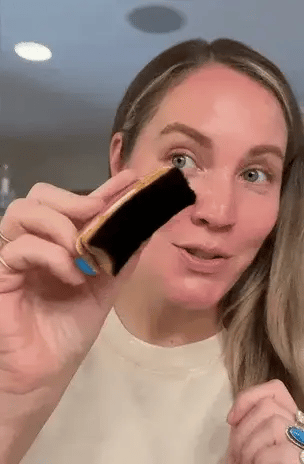 Woman holding a Clara Contour brush near her face in a bathroom setting